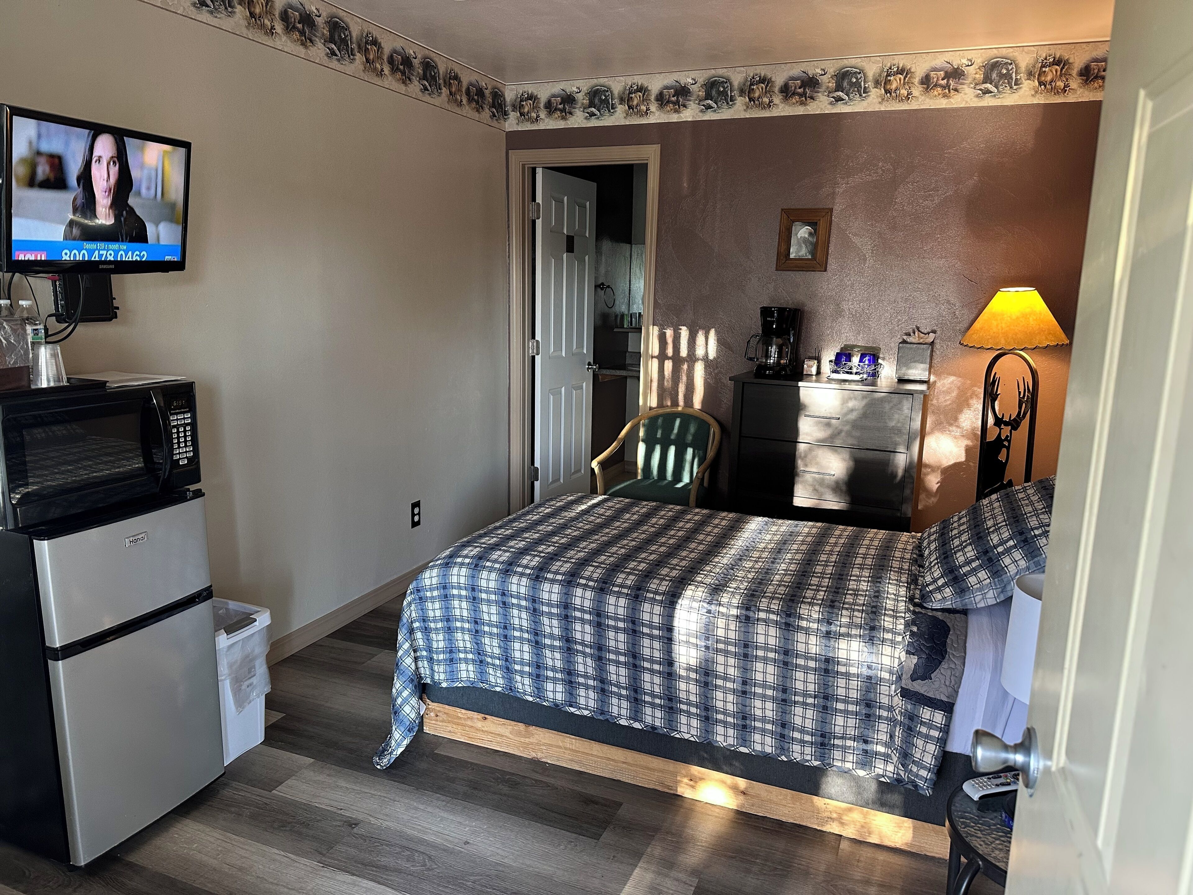 A compact hotel room with a bed, a desk with a computer, a microwave, and a coffee maker.