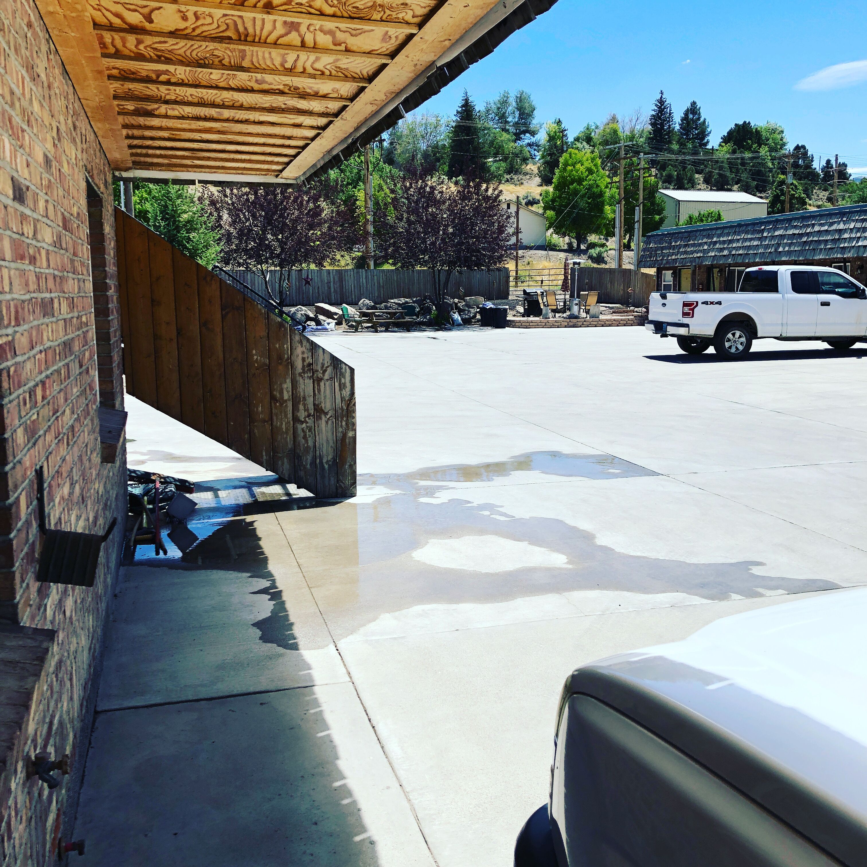 Un estacionamiento con una camioneta pickup blanca, una estructura de madera cubierta y un edificio de ladrillo.