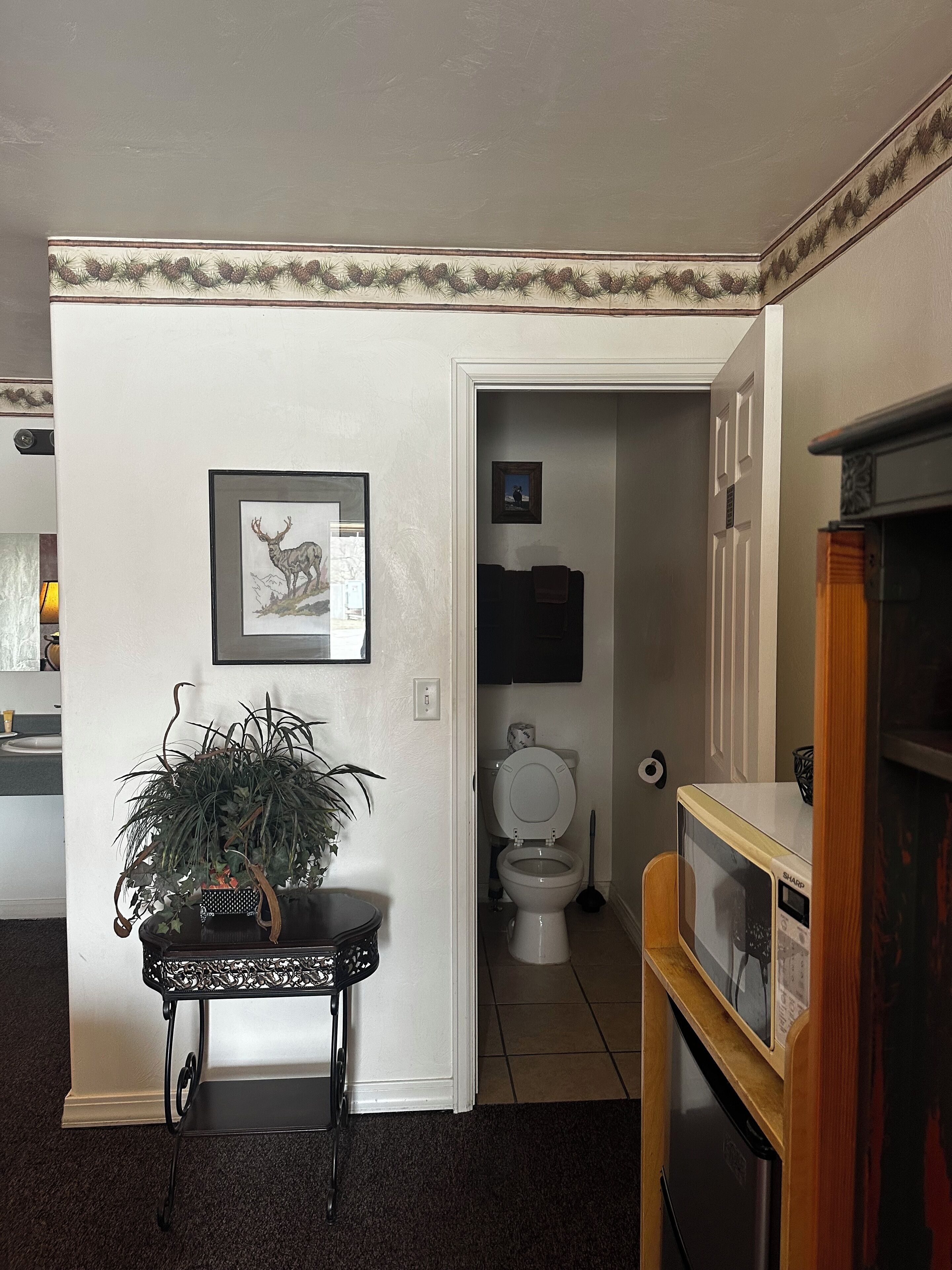Ein Badezimmer mit Toilette, Waschbecken und Spiegel. An der Wand hängt ein gerahmtes Bild und auf einem Tisch steht ein Blumentopf.