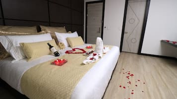 Una habitación de hotel con una cama bien hecha, una botella de champán, pétalos de rosa y una vela sobre la cama.