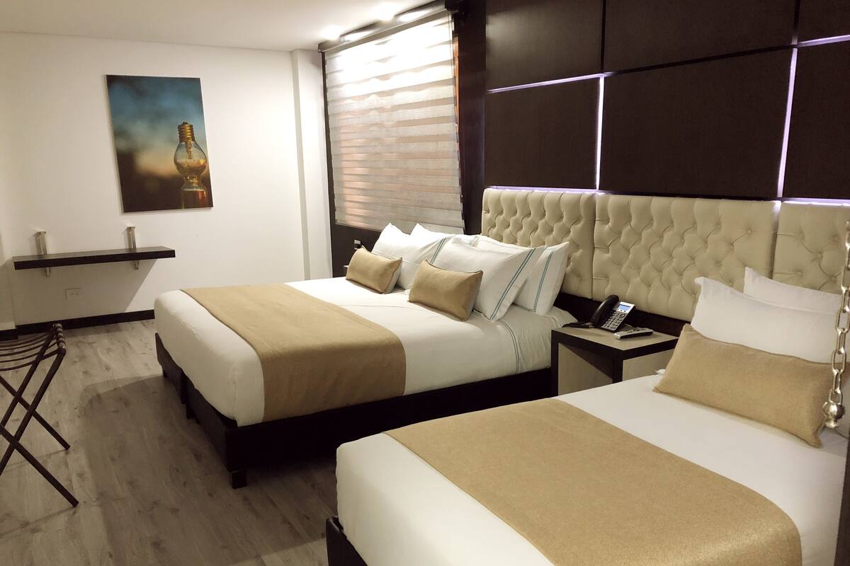 Hotelkamer met twee bedden, een nachtkastje met telefoon, een schilderij aan de muur en een raam met luxaflex.
