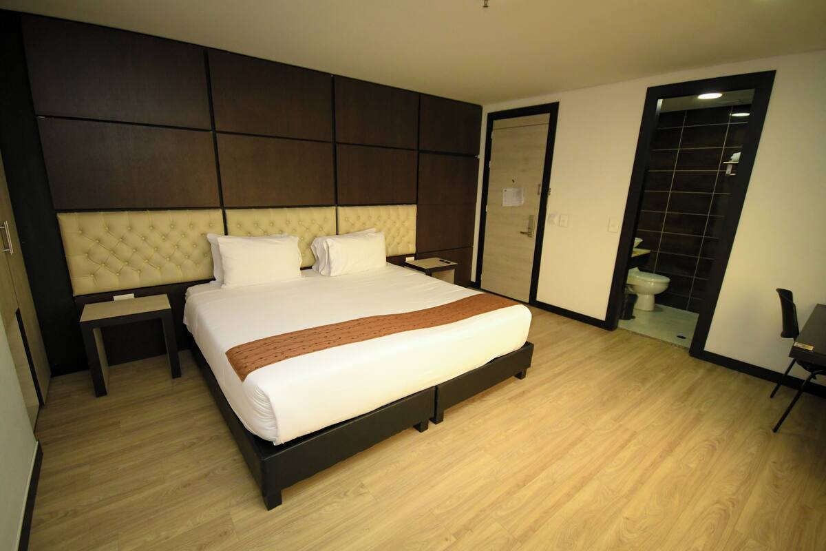 Een moderne hotelkamer met een groot bed, een nachtkastje, een kledingkast en een badkamer die door een open deur zichtbaar is.