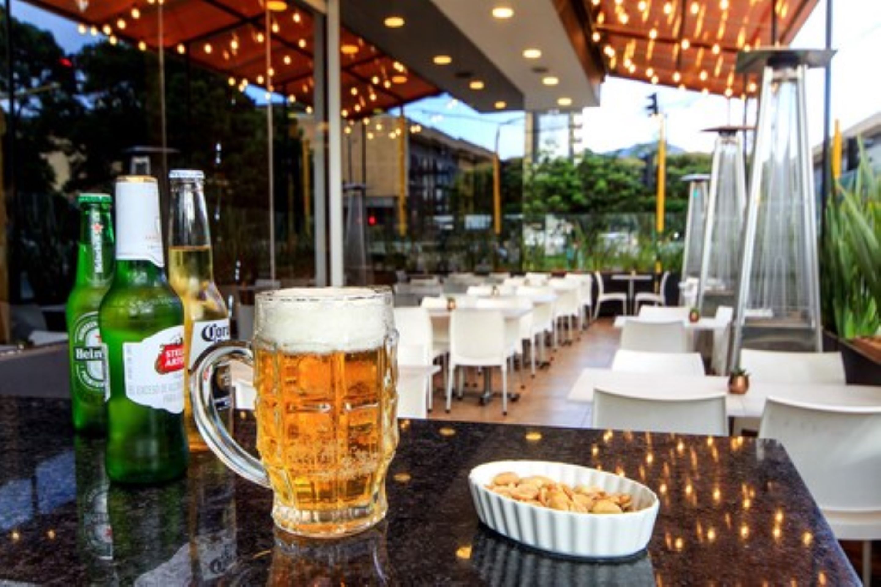 Un espacio de comedor al aire libre con mesas y sillas, una jarra de cerveza y botellas de cerveza.