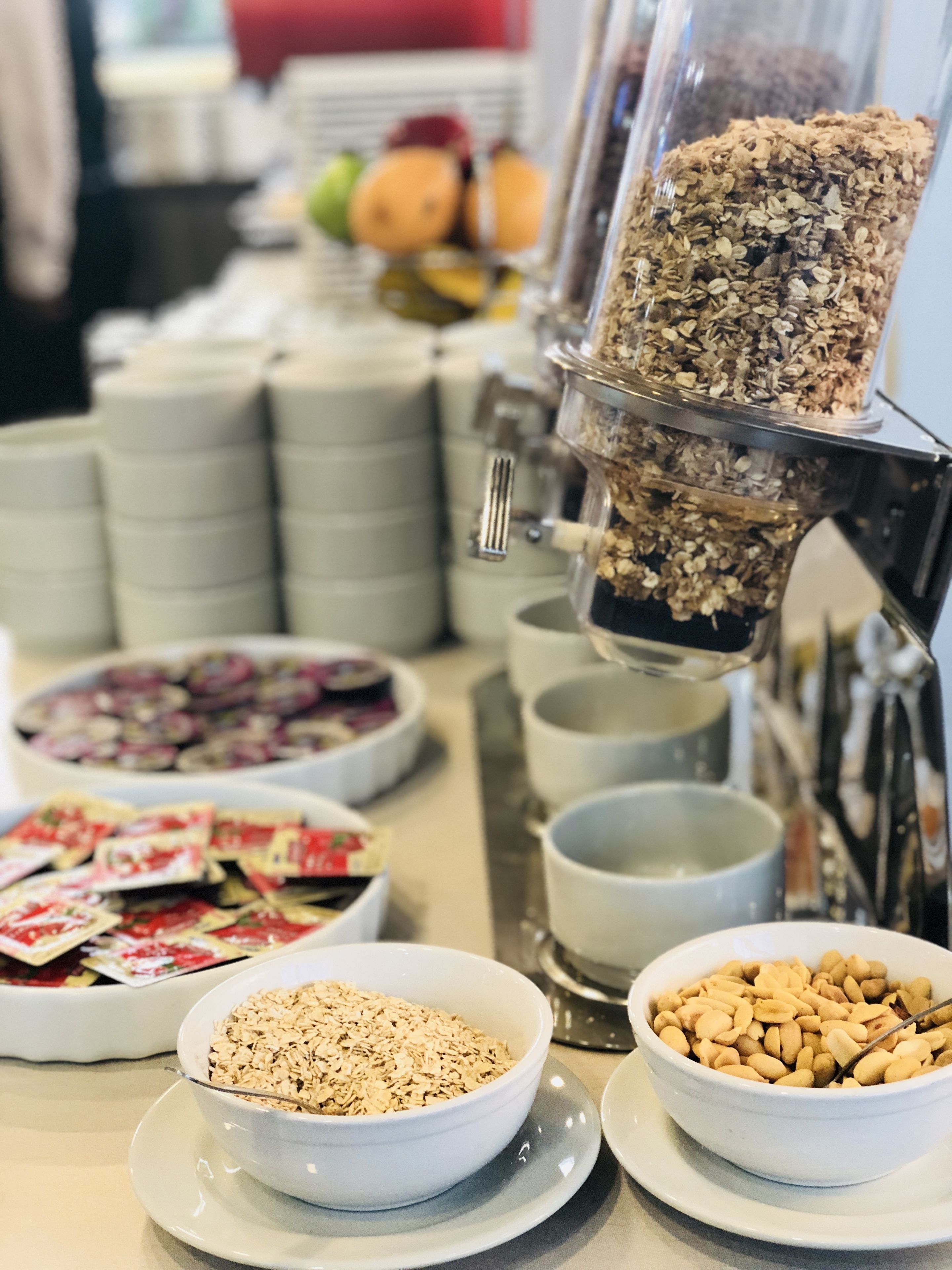 Montaje tipo bufé con diversos alimentos, incluyendo tazones de cereales, frutos secos y una máquina de café.