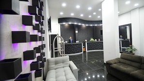 A modern reception area with a curved black reception desk, a grey sofa, and a green sofa.