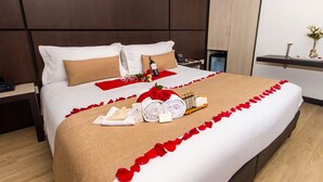 A neatly made bed with a red rose, a towel, and toiletries.