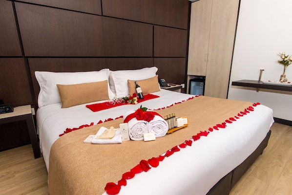 Una cama bien hecha con una rosa roja, una toalla y artículos de aseo.