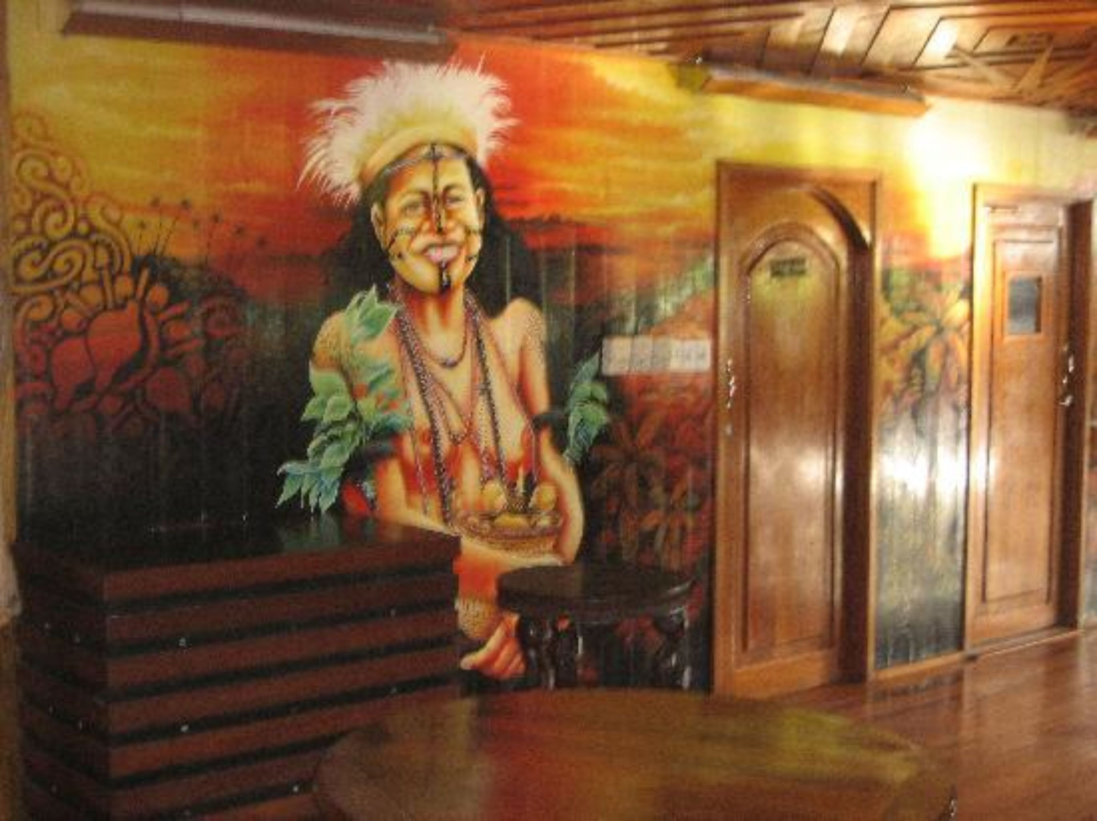 A mural of a person with a feathered headdress and a necklace, a wooden bench, and a door in a room with patterned walls.