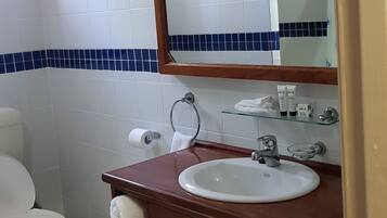 A bathroom with a white toilet, a wooden vanity with a sink, a mirror, and a glass shelf with toiletries.