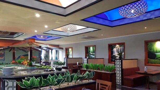 Ein modernes Restaurant mit Barbereich, Sitzgelegenheiten mit Pflanzen und einer Decke mit geometrischer Leuchte.