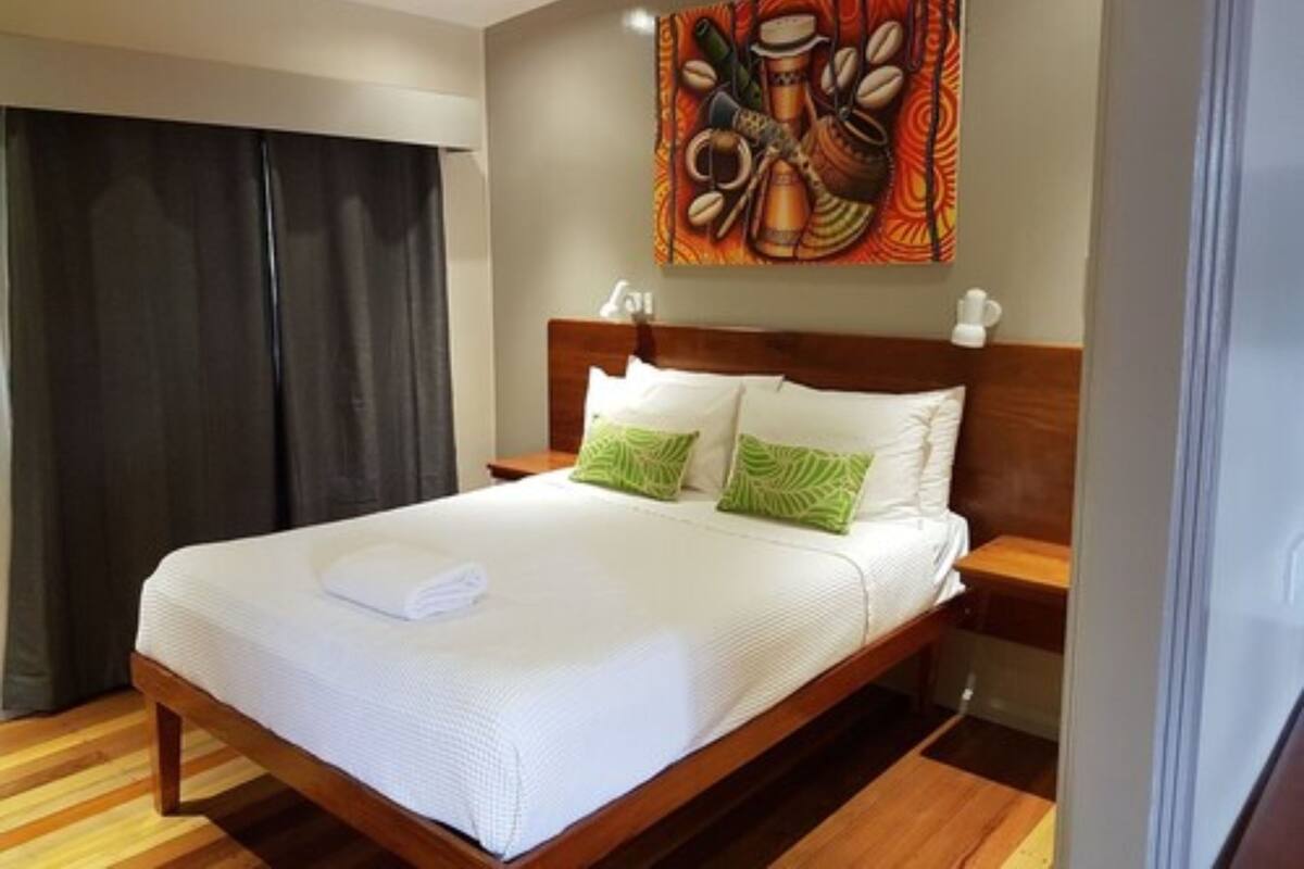 A neatly made bed with white linens, a wooden headboard, and two green pillows.