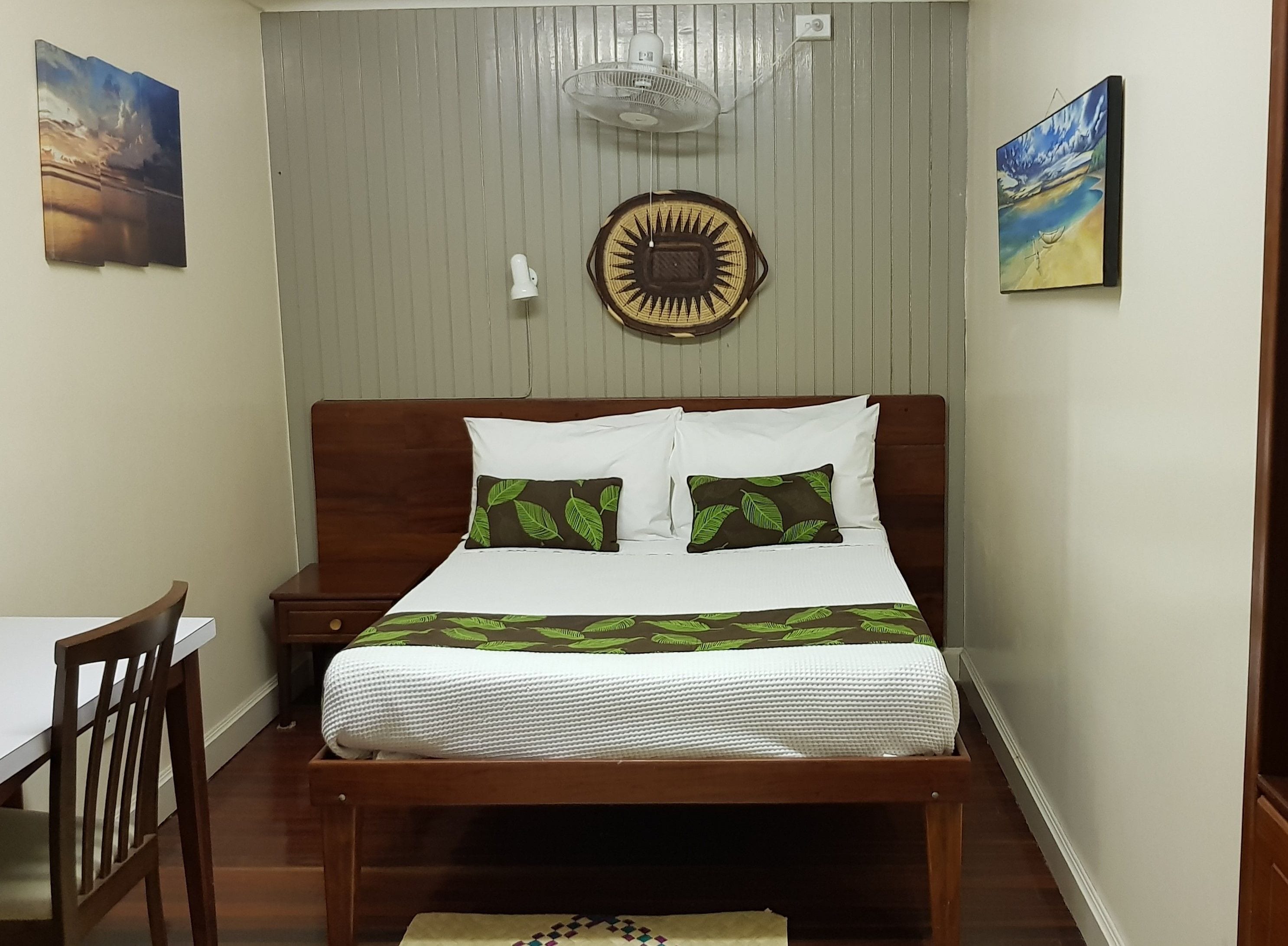 A neatly arranged bedroom with a wooden bed, white bedding, and green leaf-patterned pillows.