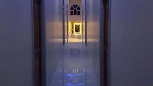 Ein langer, schmaler Gang mit spiegelndem Boden und blauer Beleuchtung an der Decke.