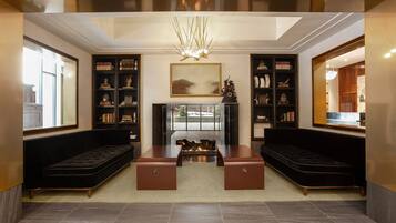 A modern living room with a fireplace, two black sofas, a coffee table, and a large bookshelf.