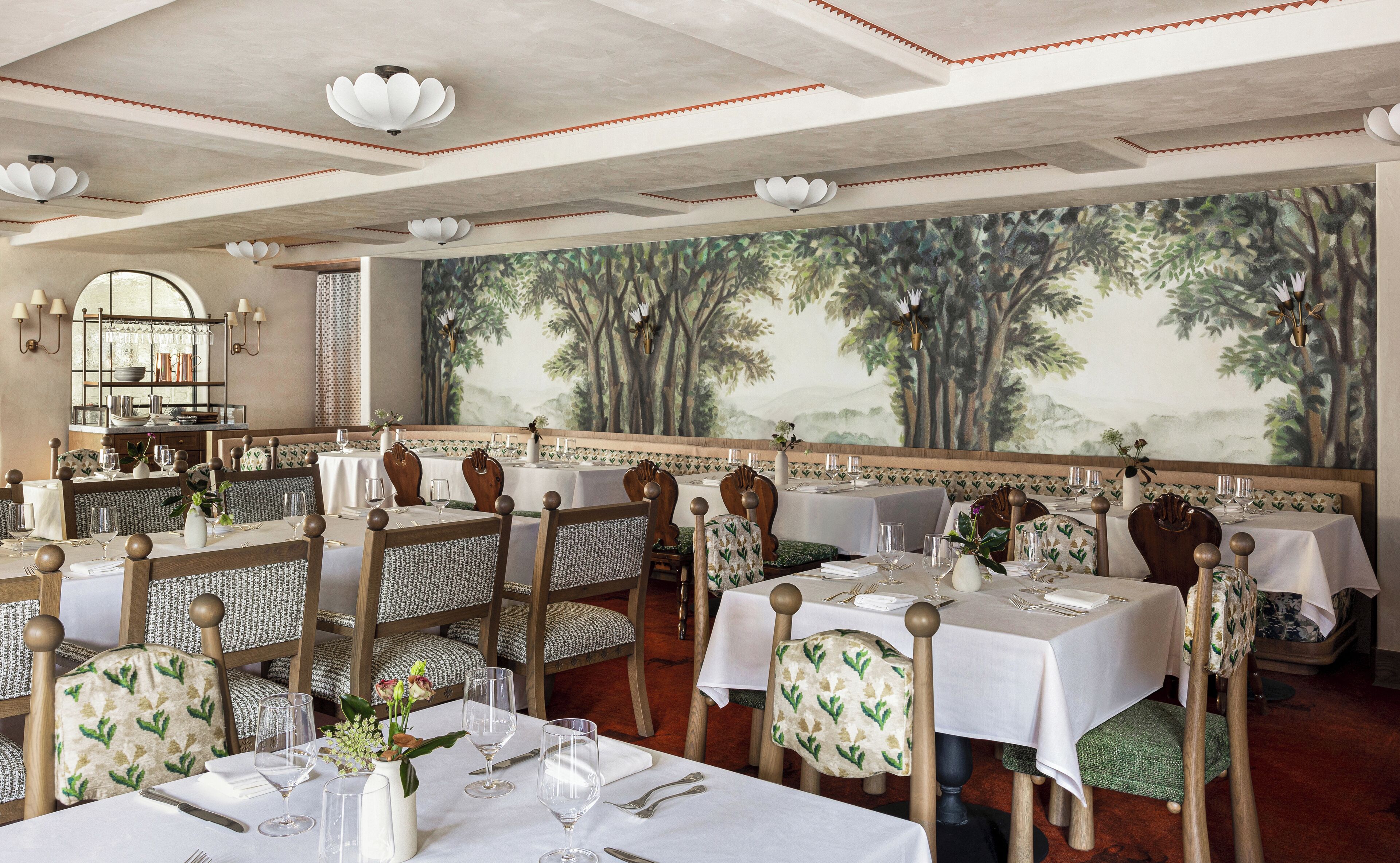 A restaurant with multiple tables and chairs, each set with white tablecloths and silverware.