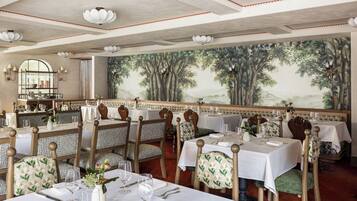 A restaurant with multiple tables and chairs, each set with white tablecloths and silverware.