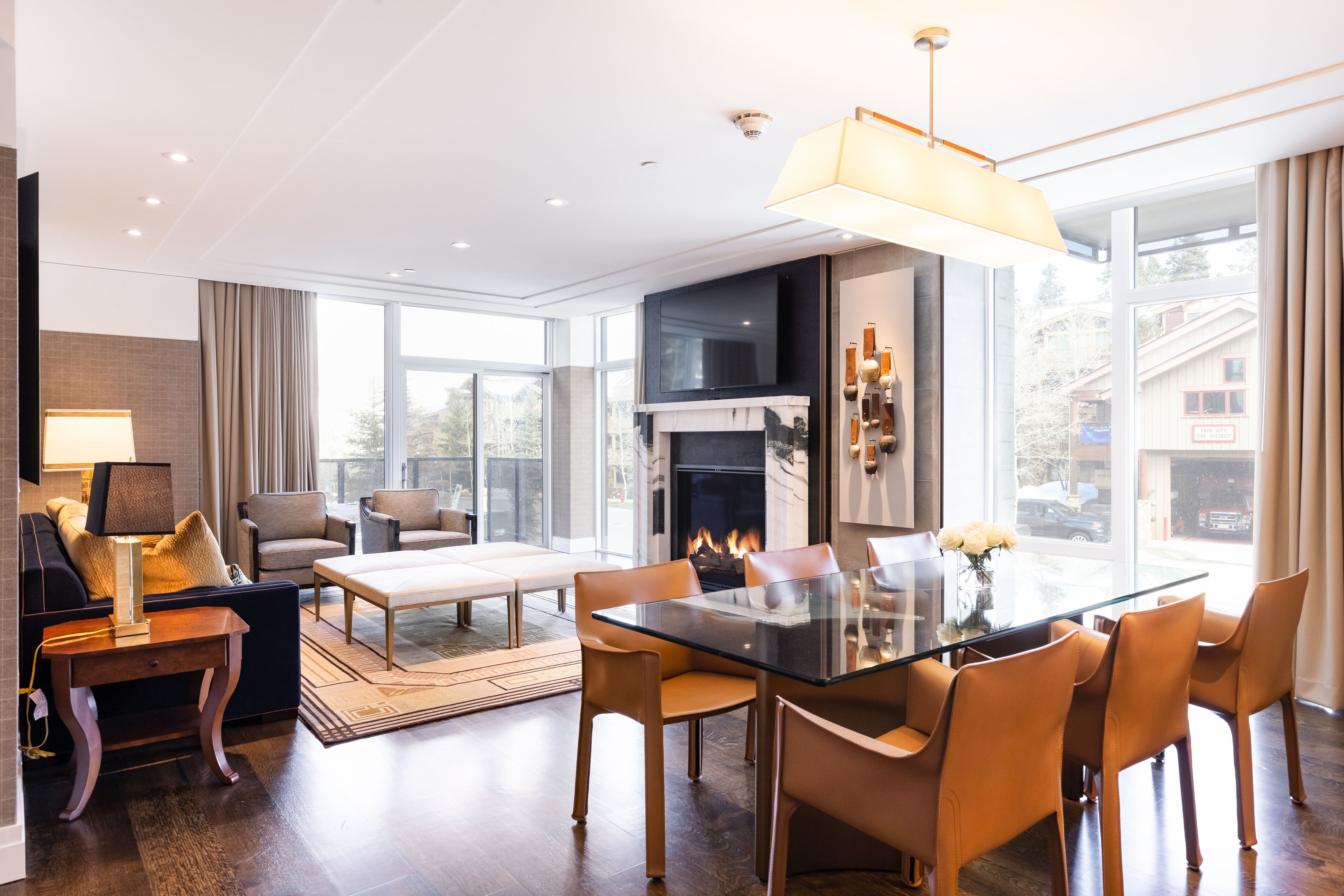 Uma sala de estar moderna com uma mesa de jantar de vidro, assentos confortáveis, lareira e grandes janelas com vista para o exterior.