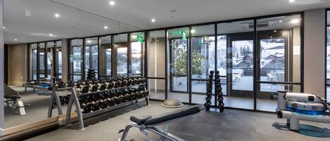 Un gimnasio moderno con equipo de ejercicio, amplias ventanas y vistas a un paisaje nevado.