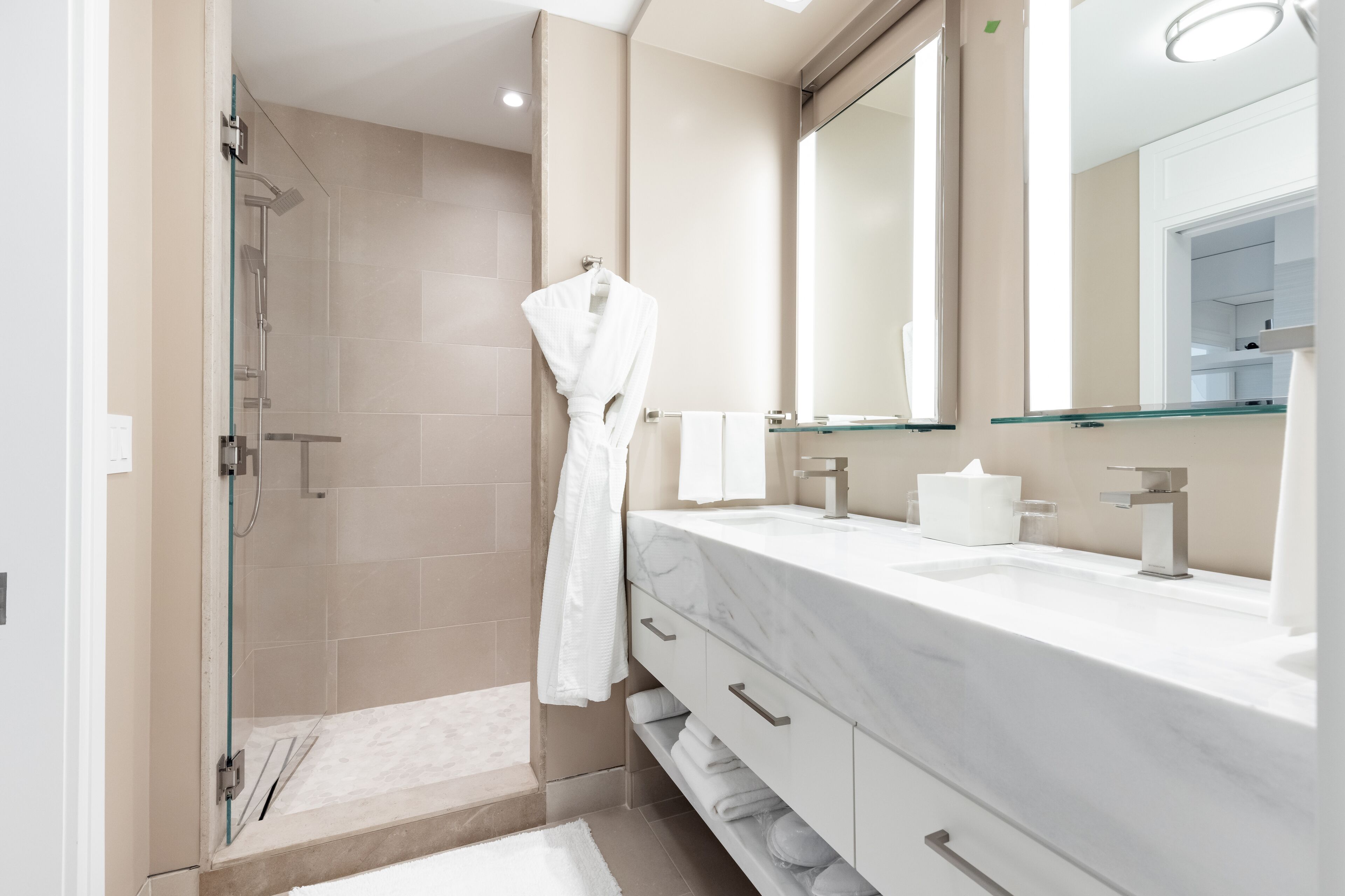 A modern bathroom with a glass-enclosed shower, a white marble vanity, and a large mirror.