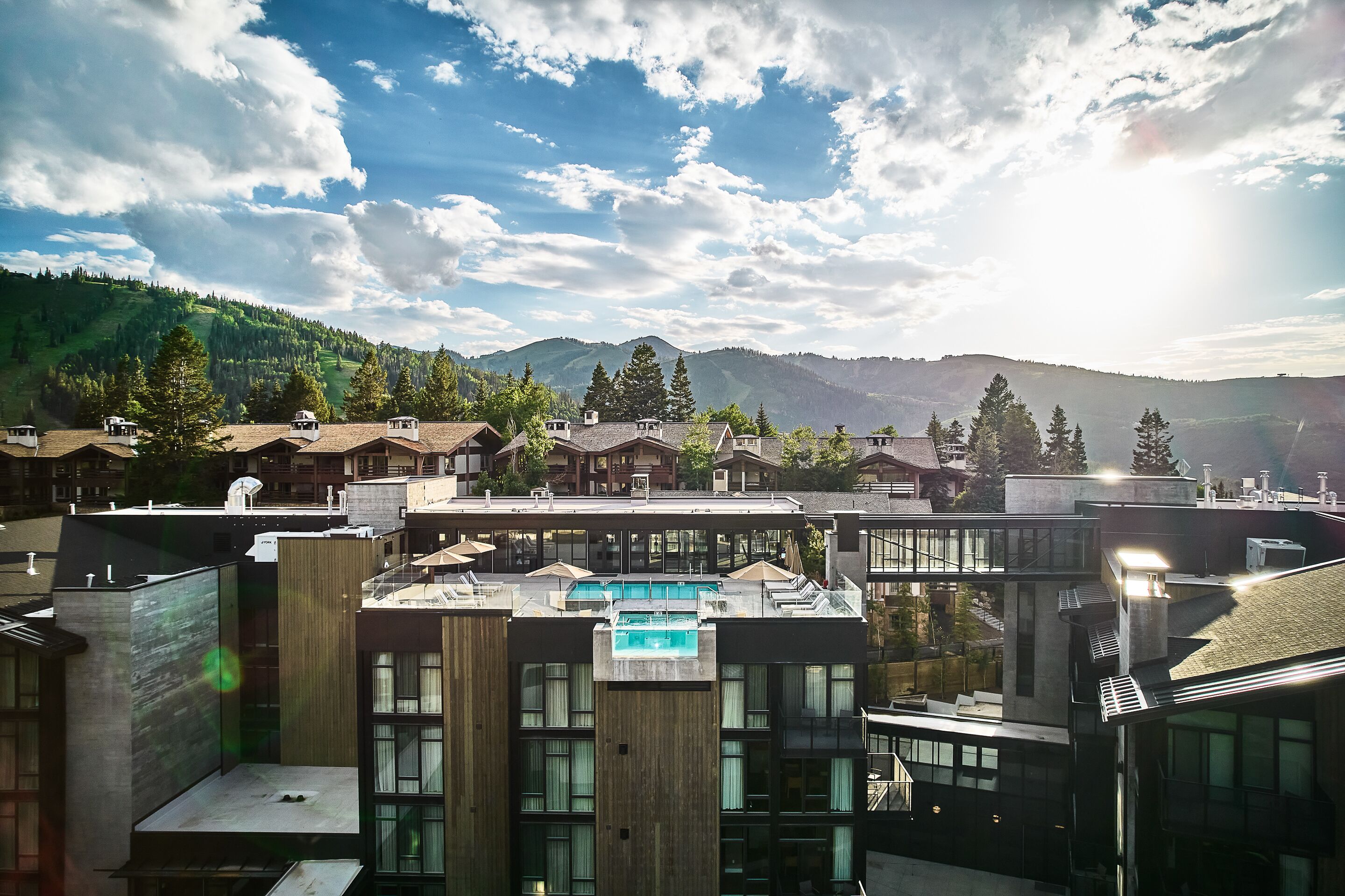Een modern hotel met een dakzwembad, omringd door bergen en bomen.