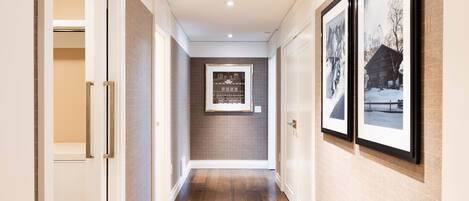 A hallway with wooden flooring, white walls, and framed pictures on the walls.