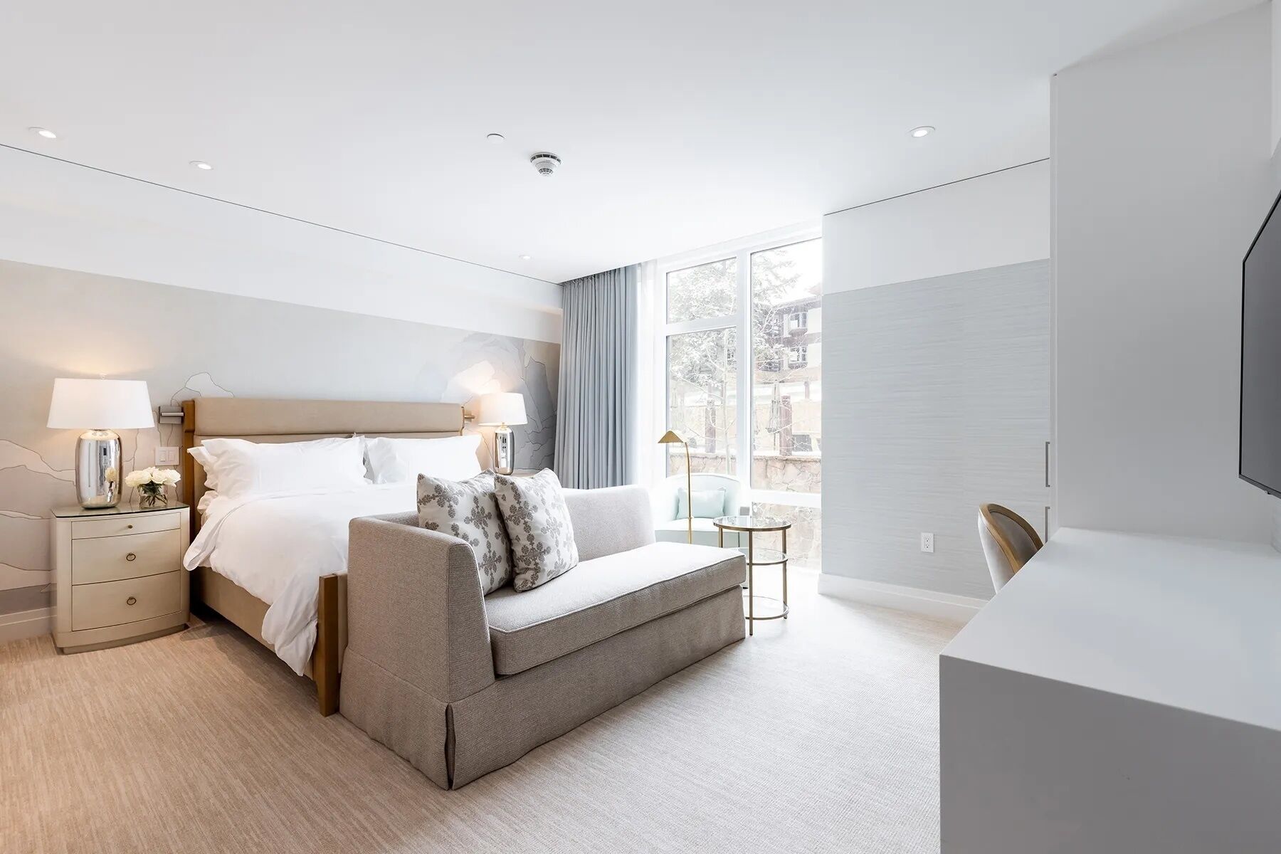 Ein modernes Schlafzimmer mit Bett, Nachttischen, einer Couch, einem Fernseher und einem Fenster mit Blick.