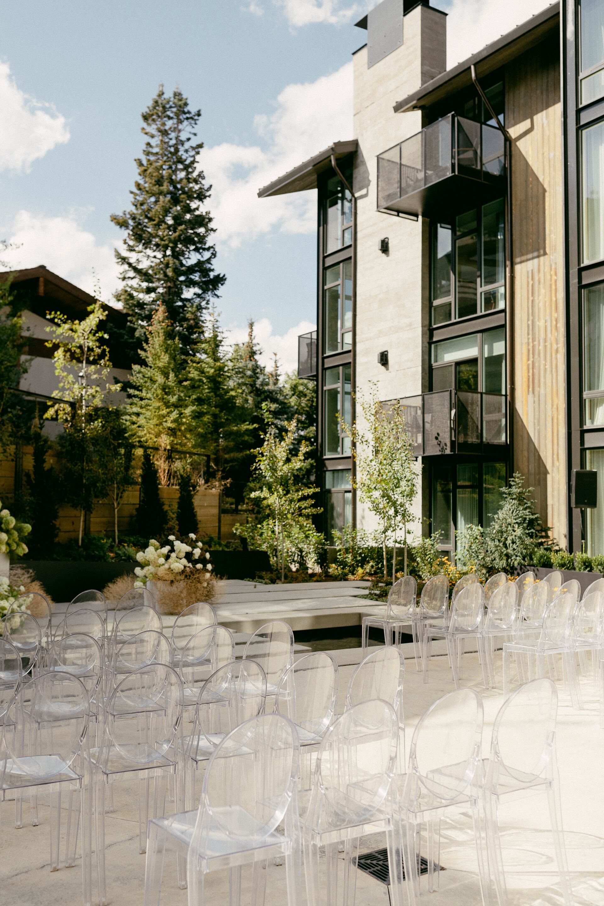 A modern building with large windows and a balcony. There are clear plastic chairs arranged in rows outside.