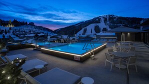 A pool area with lounge chairs and tables, surrounded by snow-covered hills and a clear sky. - Goldener Hirsch, Auberge Collection (Park City)