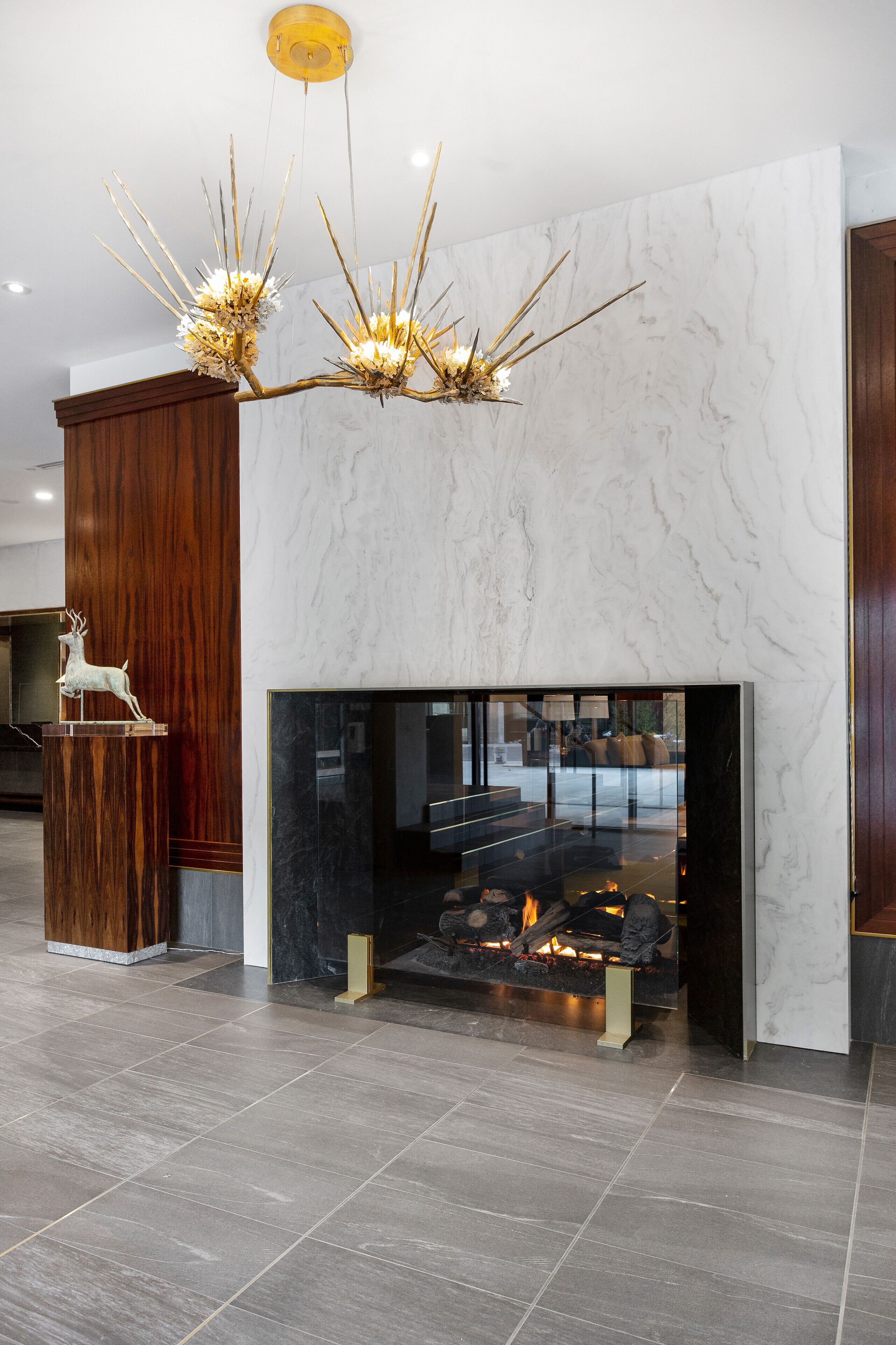 A modern lobby with a marble fireplace, a wooden sculpture, and a unique chandelier.