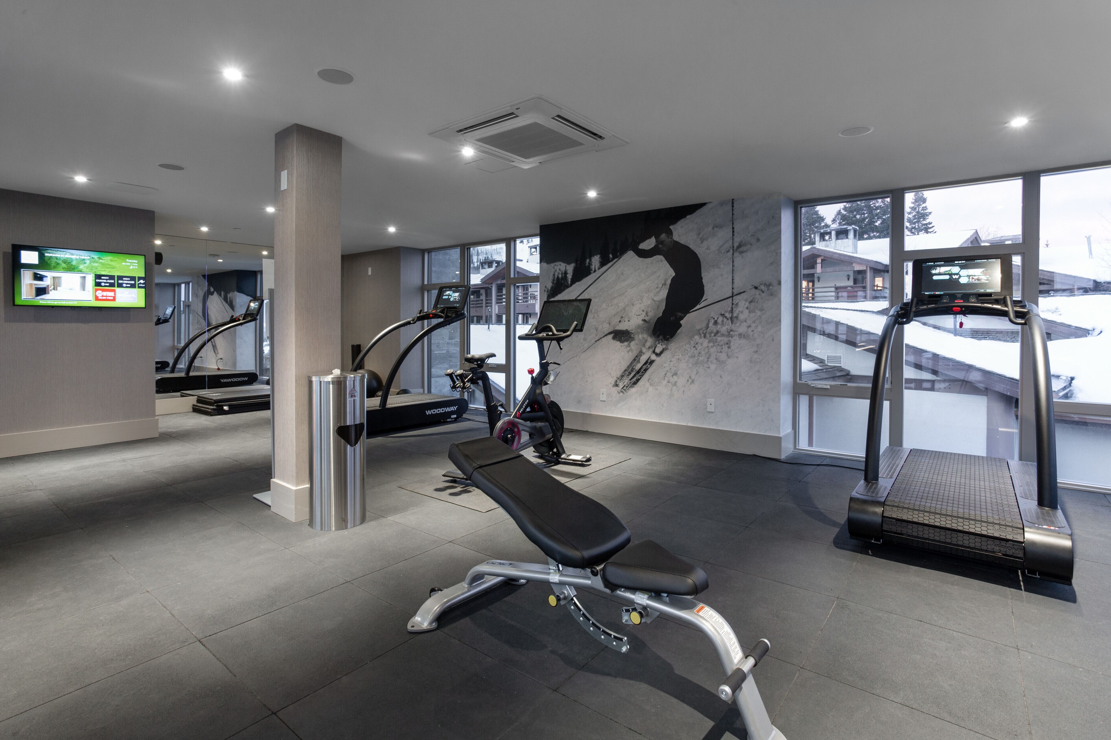 A modern gym with treadmills, a bench, and a large window offering a view of the outside.