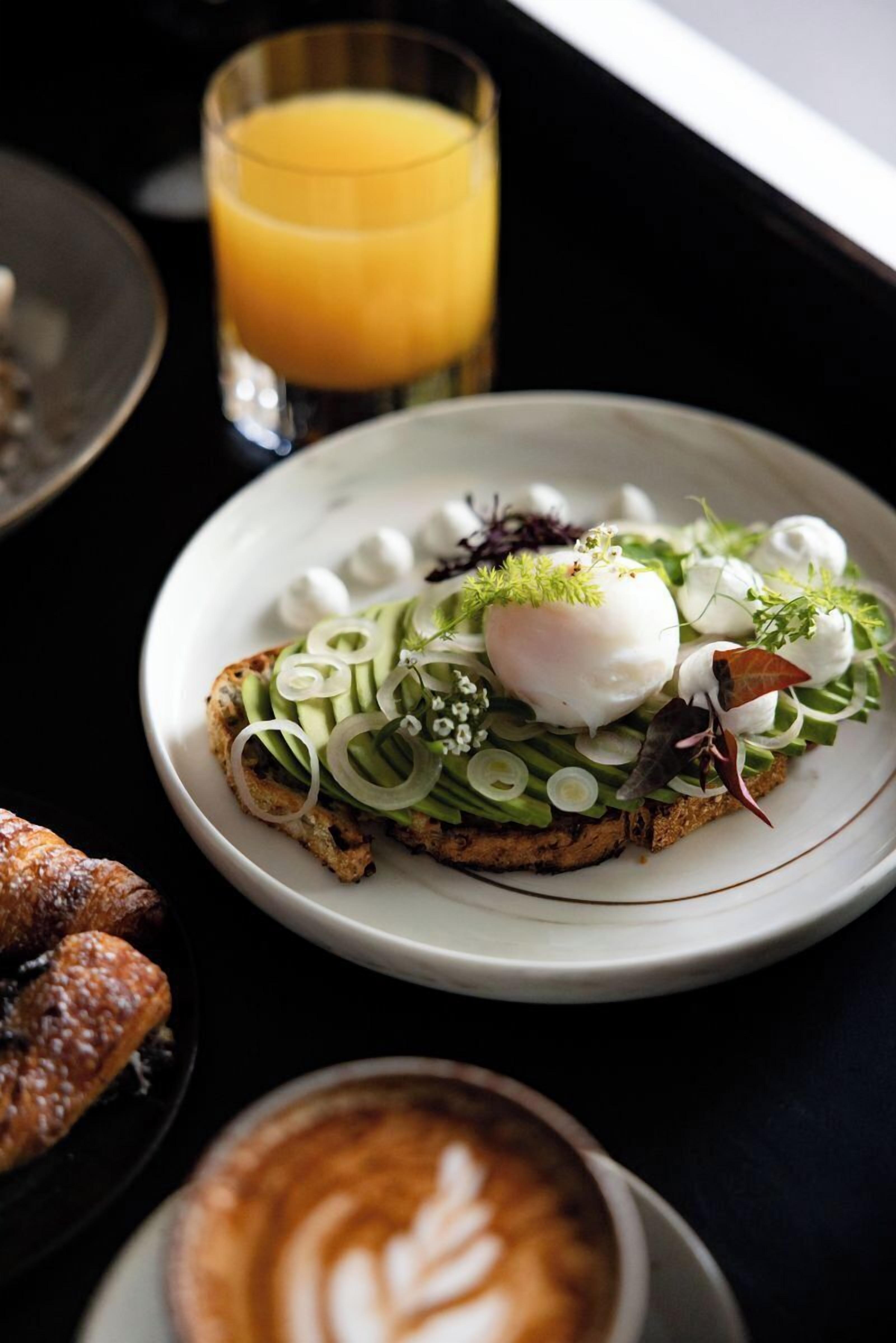 En tallerken med mad bestående af pocheret æg, avocado og grønt, serveret med et glas appelsinjuice og en latte med latte-kunst.