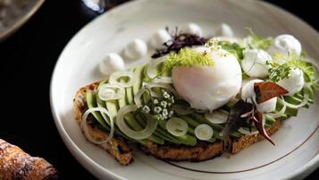 A plate of food with a poached egg, avocado, and greens, accompanied by a glass of orange juice and a latte with latte art.