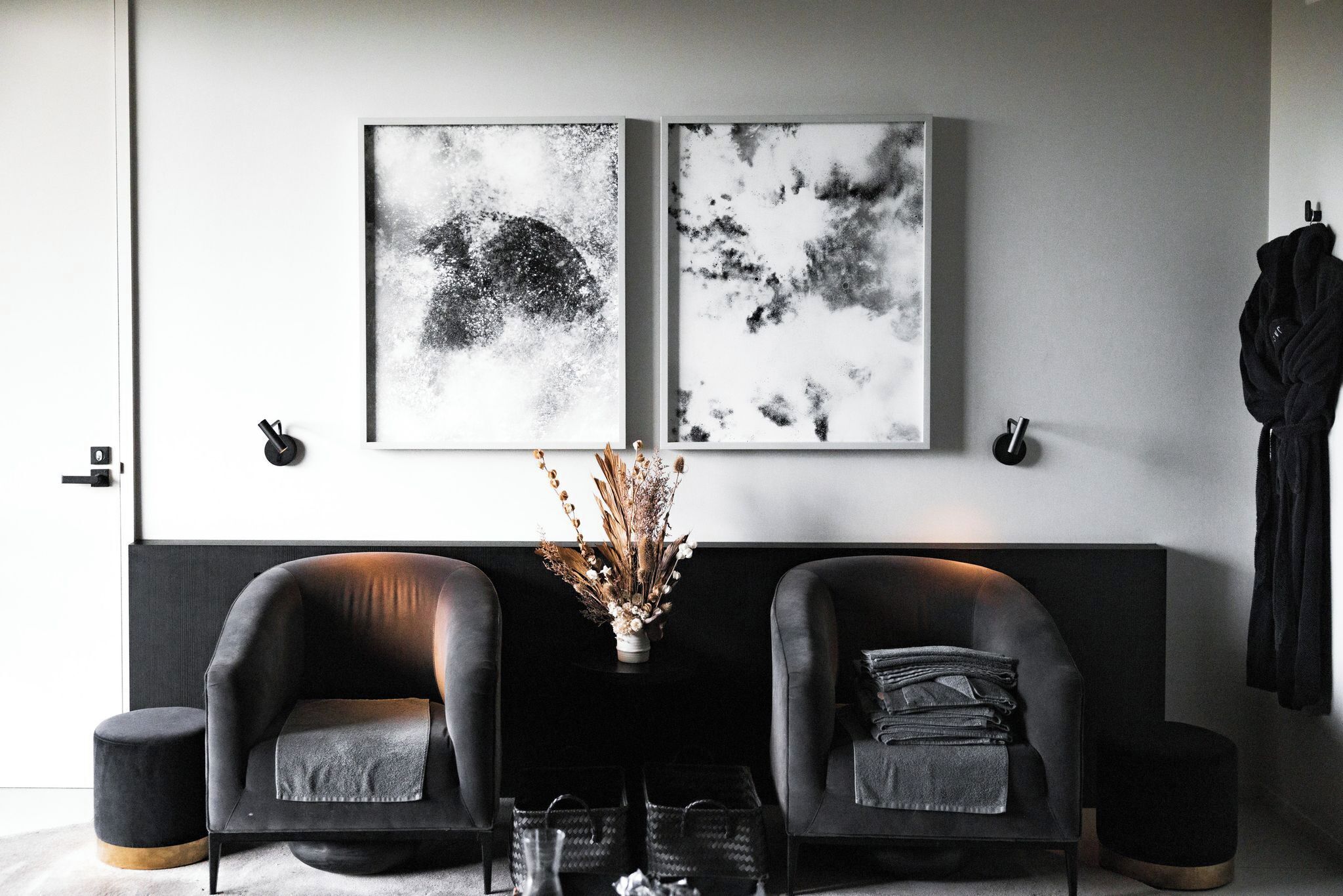 Una sala moderna con dos sofás de cuero negro, una mesita con un jarrón de plantas secas y dos cuadros abstractos en blanco y negro en la pared.