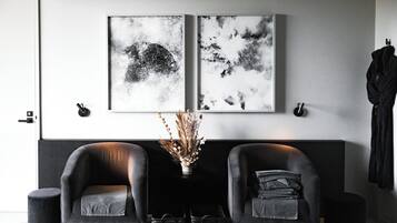 Una sala moderna con dos sofás de cuero negro, una mesita con un jarrón de plantas secas y dos cuadros abstractos en blanco y negro en la pared.
