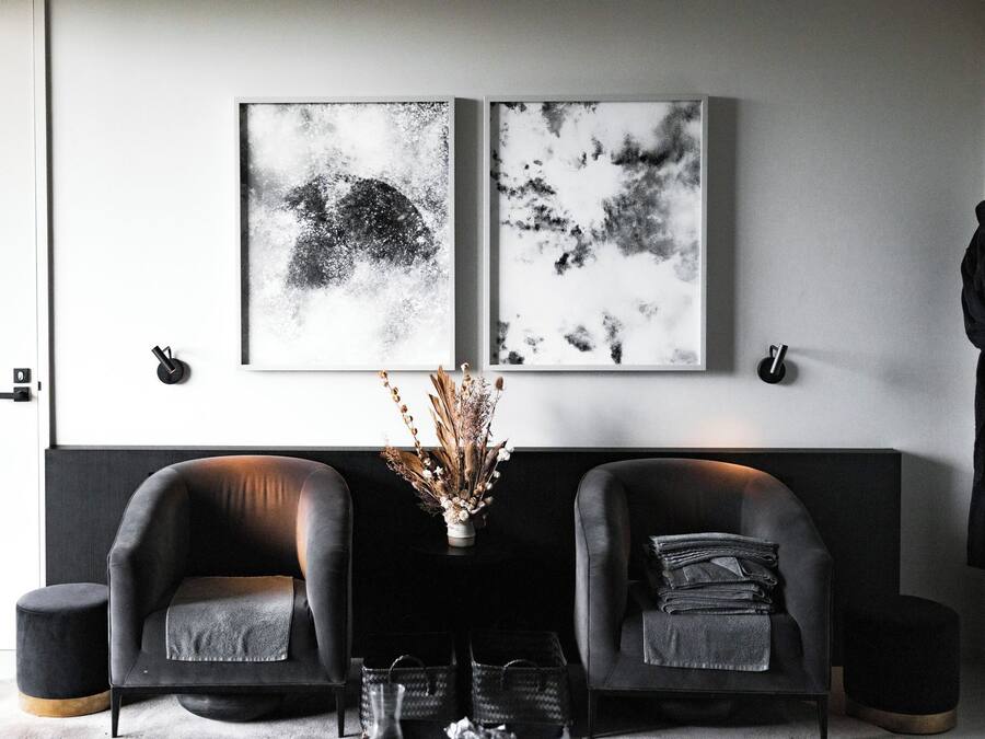 Una sala moderna con dos sofás de cuero negro, una mesita con un jarrón de plantas secas y dos cuadros abstractos en blanco y negro en la pared.