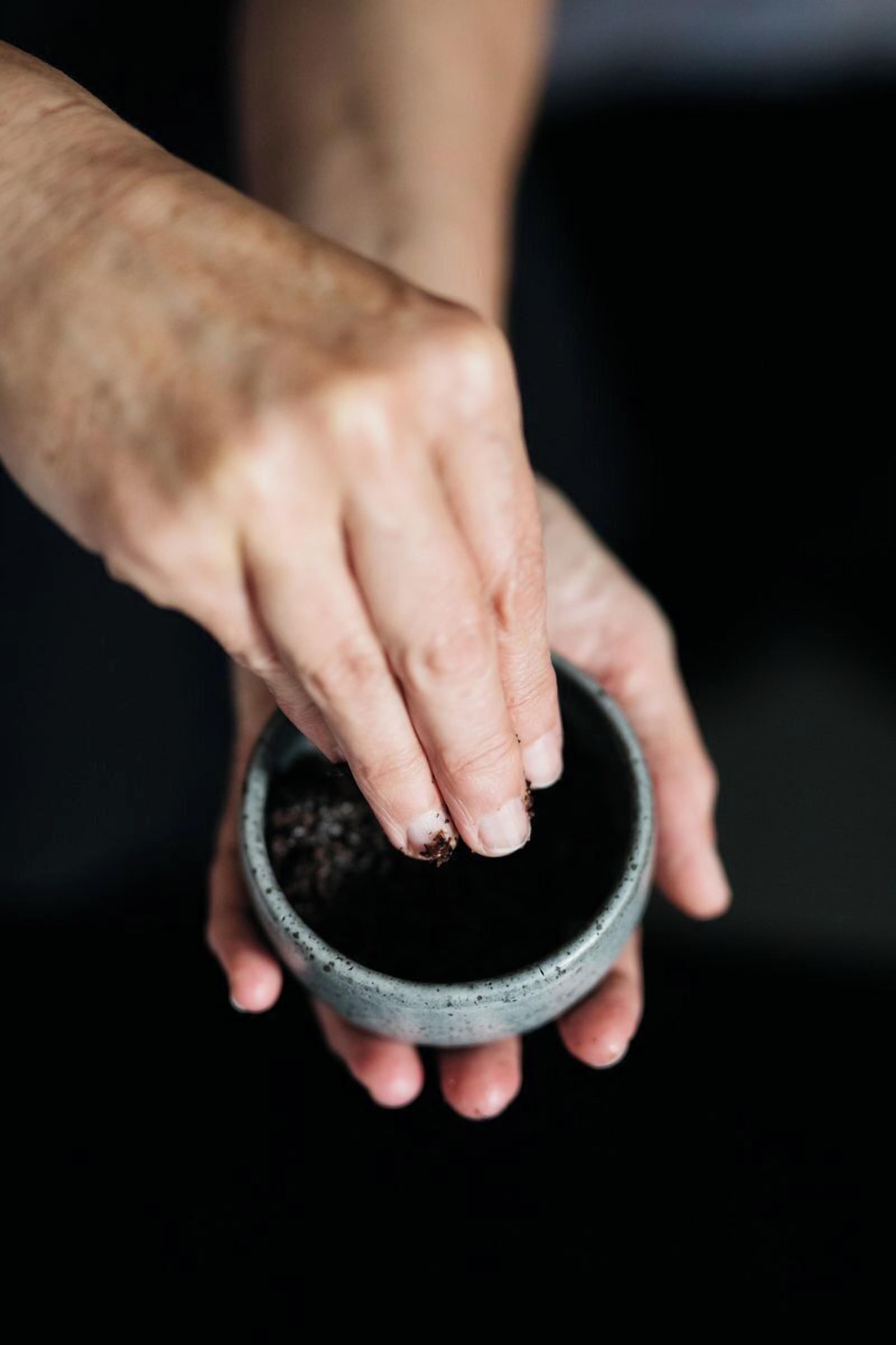 A person holding a small, dark-colored bowl with soil.