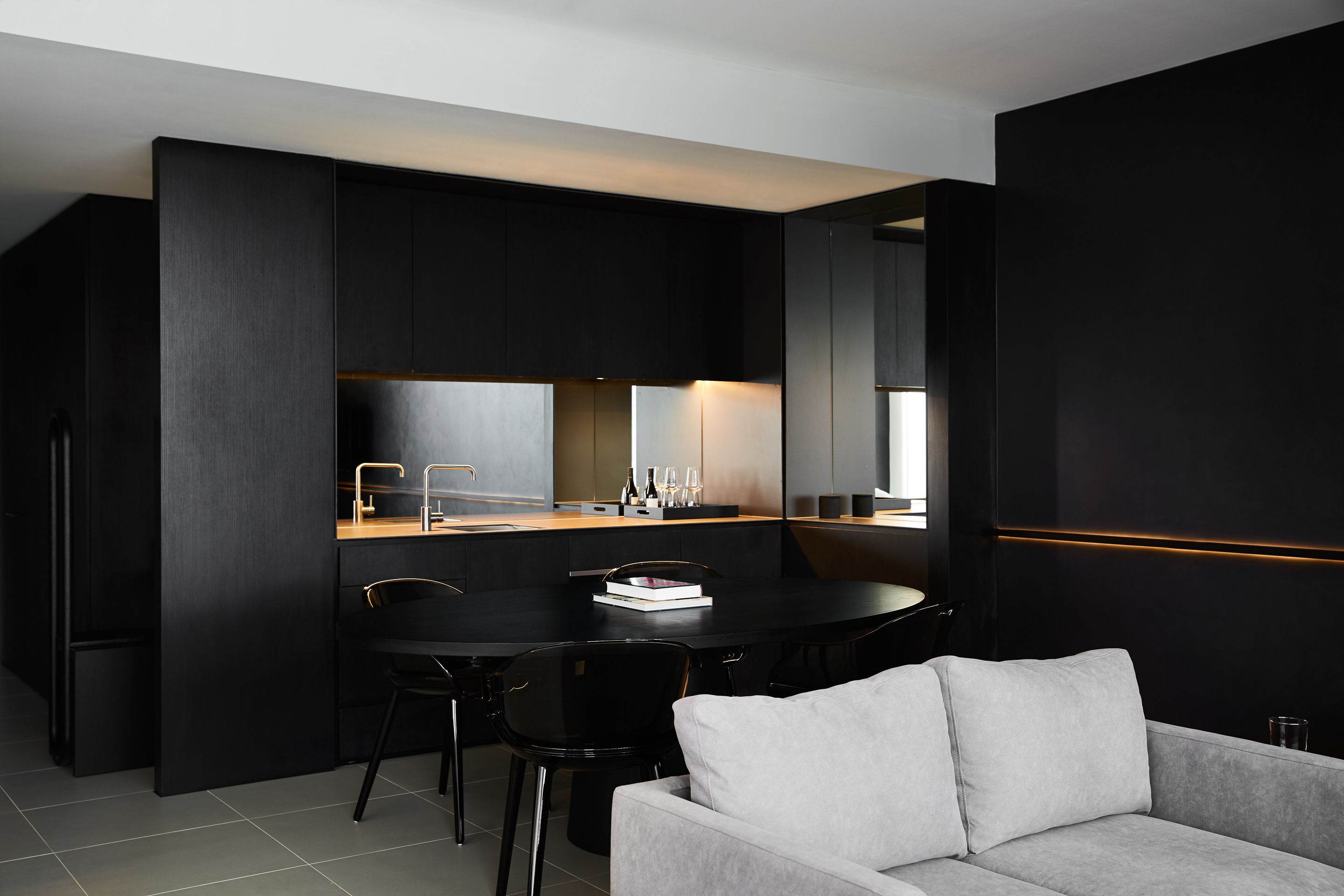 A modern kitchen with dark cabinetry, a dining table with chairs, and a light-colored sofa in a contemporary living area.