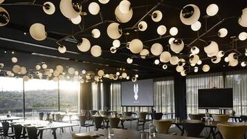 Een moderne congreszaal met een panoramisch uitzicht, met een uniek plafondontwerp inclusief sferische lampen en een groot scherm waarop een logo wordt weergegeven.
