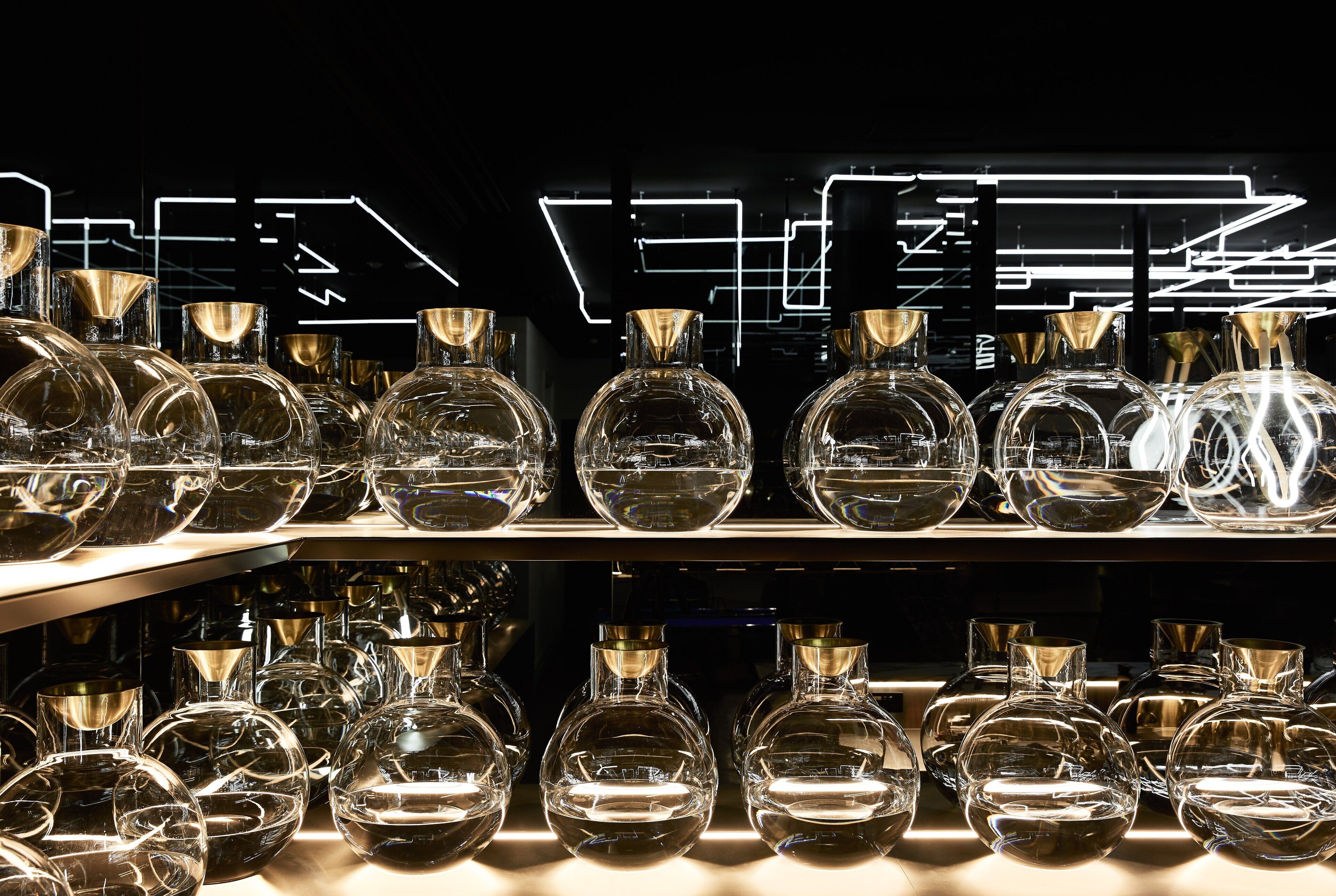 A display of clear glass bottles on shelves with a modern, illuminated background.