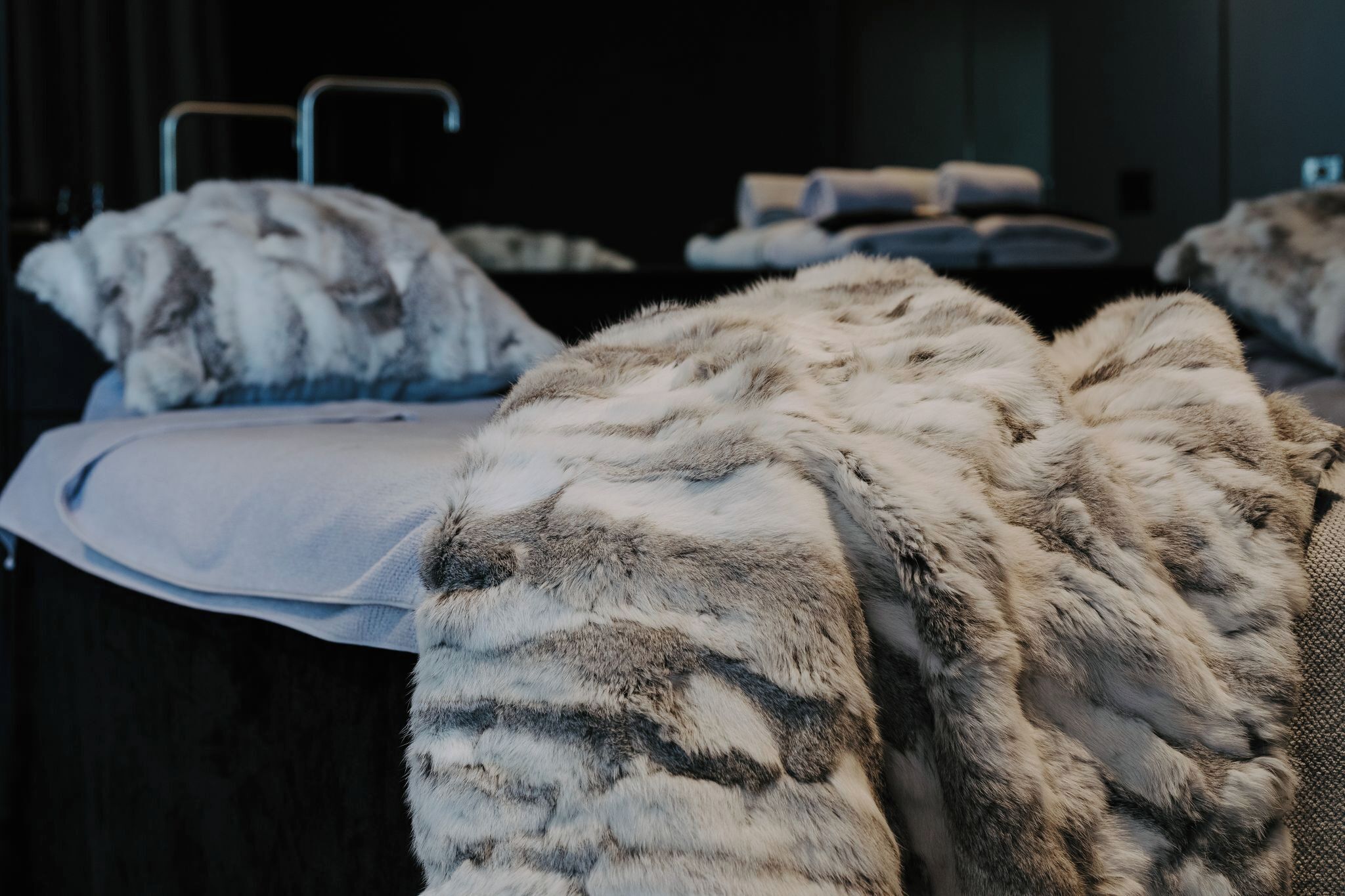 A hotel room with a bed covered in a fluffy, patterned blanket, a bedside table, and a dark wooden headboard.