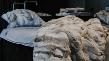 A hotel room with a bed covered in a fluffy, patterned blanket, a bedside table, and a dark wooden headboard.