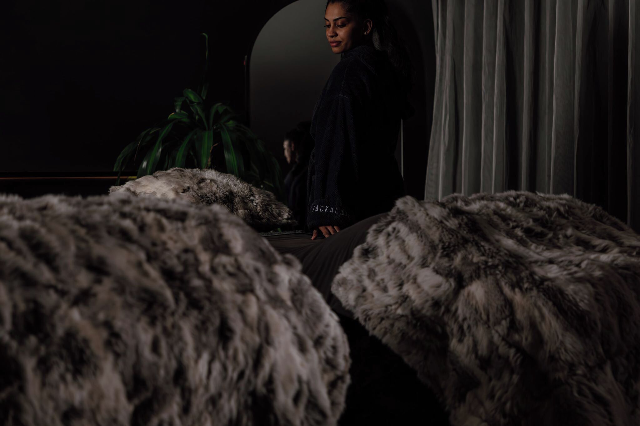 A dimly lit room with a person seated at a table, surrounded by large, fluffy, grey sofas.
