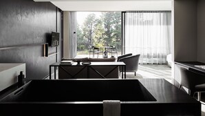 A modern hotel room with a large bathtub, a dining area with a table and chairs, and a balcony with a view of trees. - Jackalope Hotel (Merricks North)