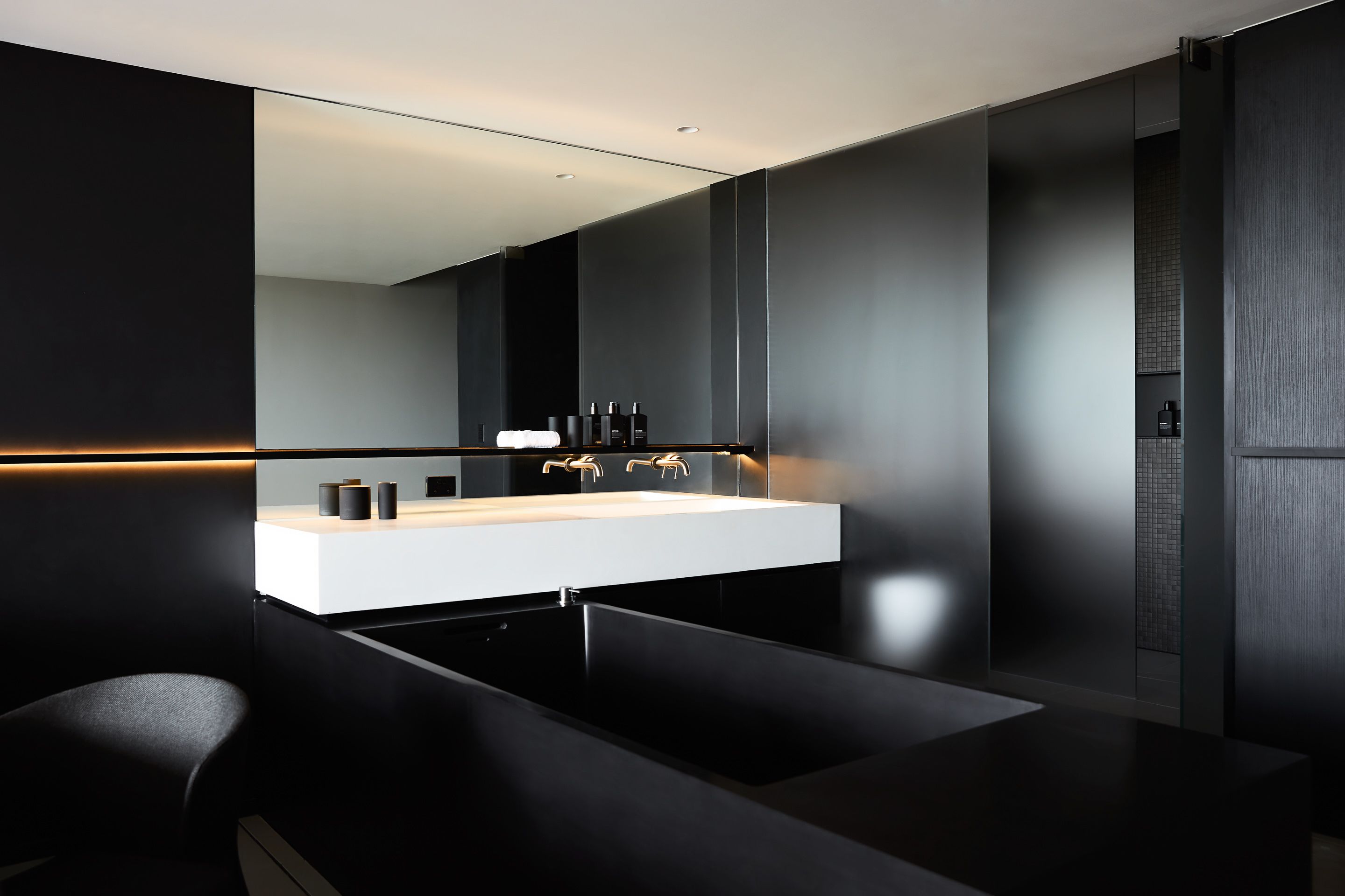 Un baño moderno con un espejo grande, un lavamanos blanco y muebles negros.