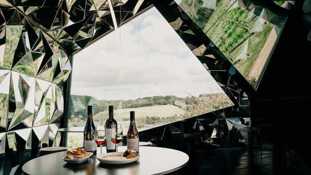 A dining table with wine bottles and glasses, set against a geometric wall with a vineyard view. - Jackalope Hotel (Merricks North)