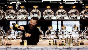 A bartender pouring a drink at a bar with a modern design, featuring multiple large glassware and bottles on shelves. - Jackalope Hotel (Merricks North)
