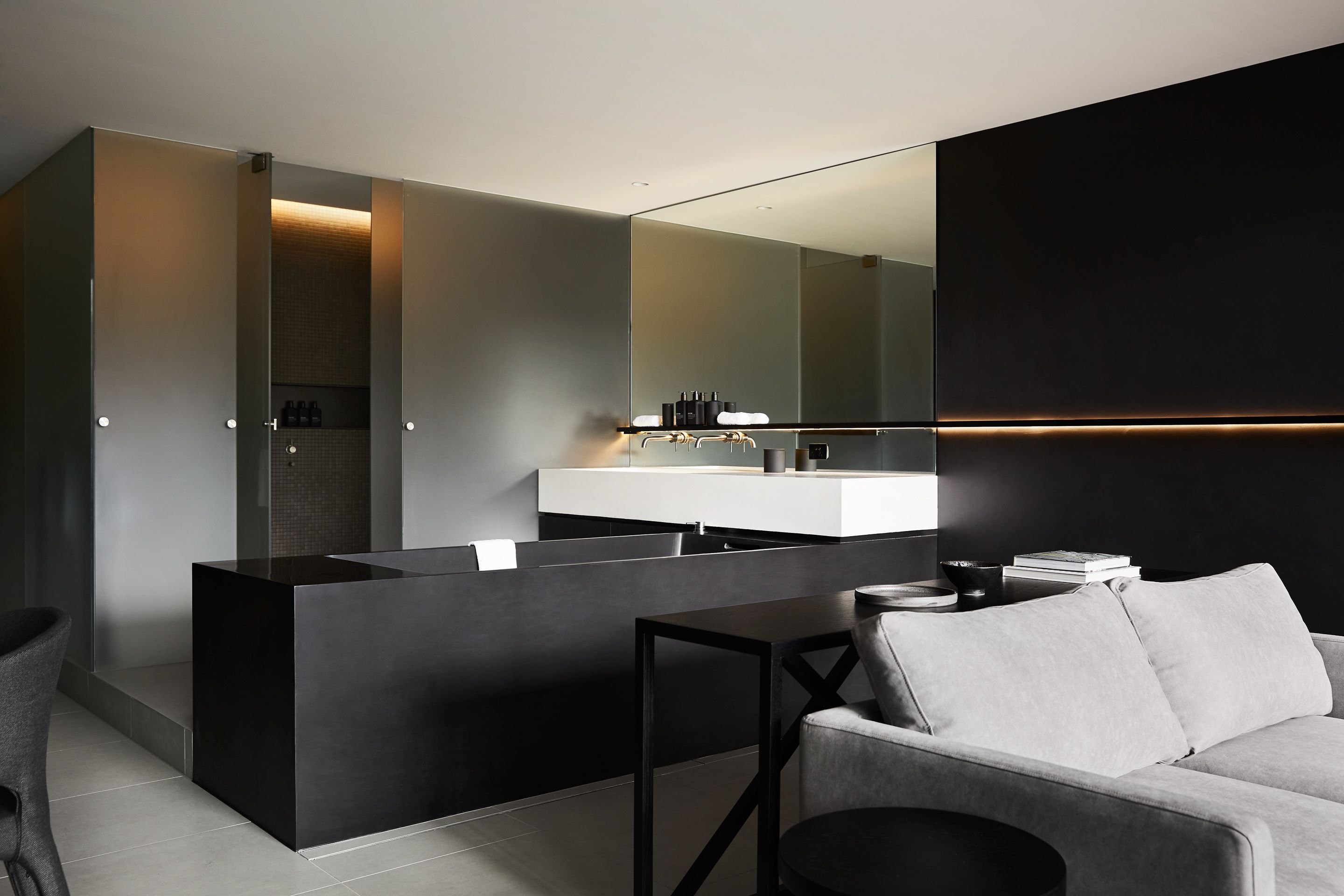 A modern bathroom with a large mirror, a dark vanity, and a grey sofa in a minimalist living area.