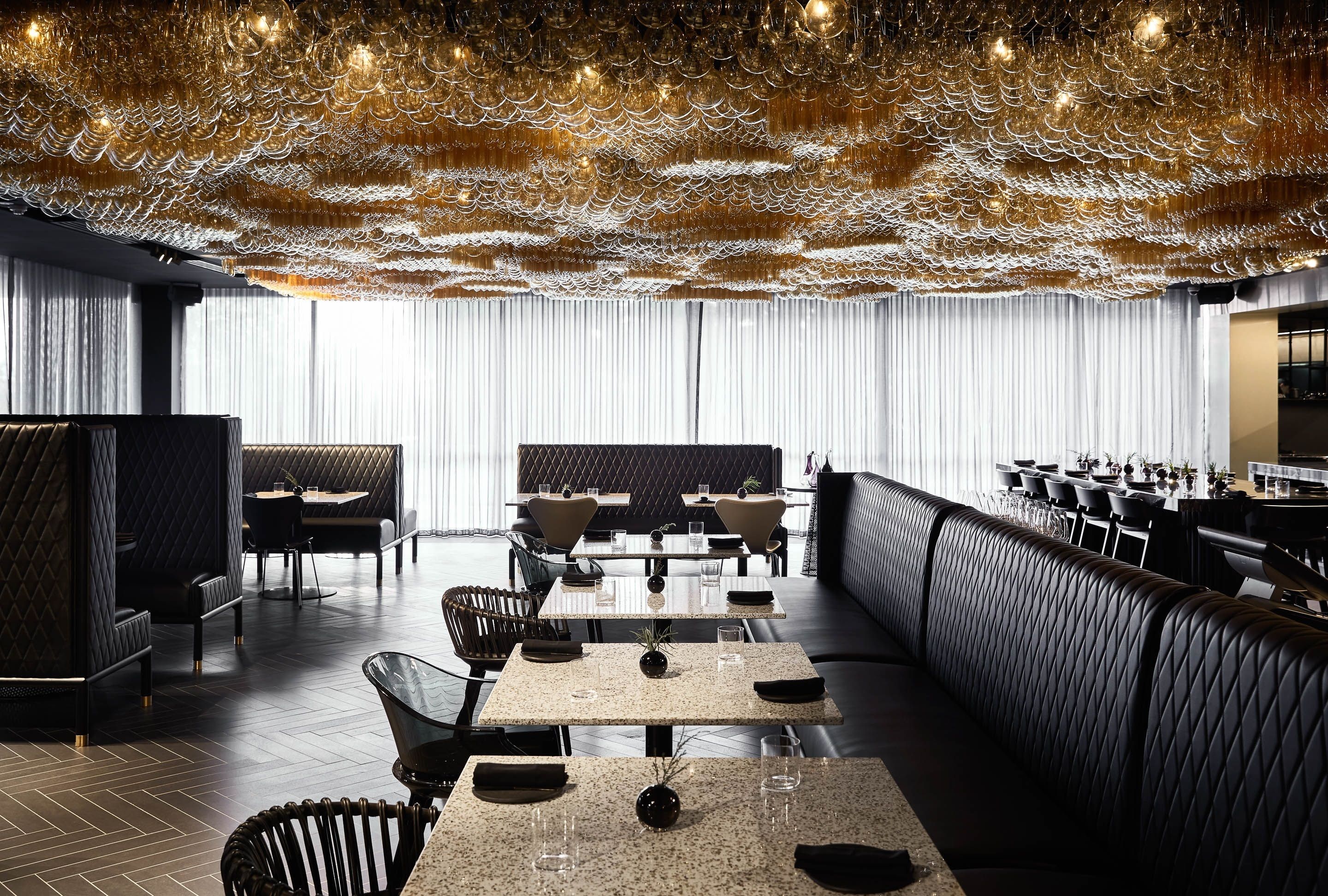 A modern restaurant with a unique ceiling design, a long dining area, and a bar.