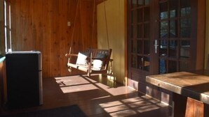 A wooden cabin interior with a swing chair, a table, and a refrigerator. - The Normaway Inn (Margaree Valley)
