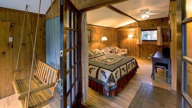 A wooden cabin bedroom with a bed, a desk, a swing, and a window. - The Normaway Inn (Margaree Valley)